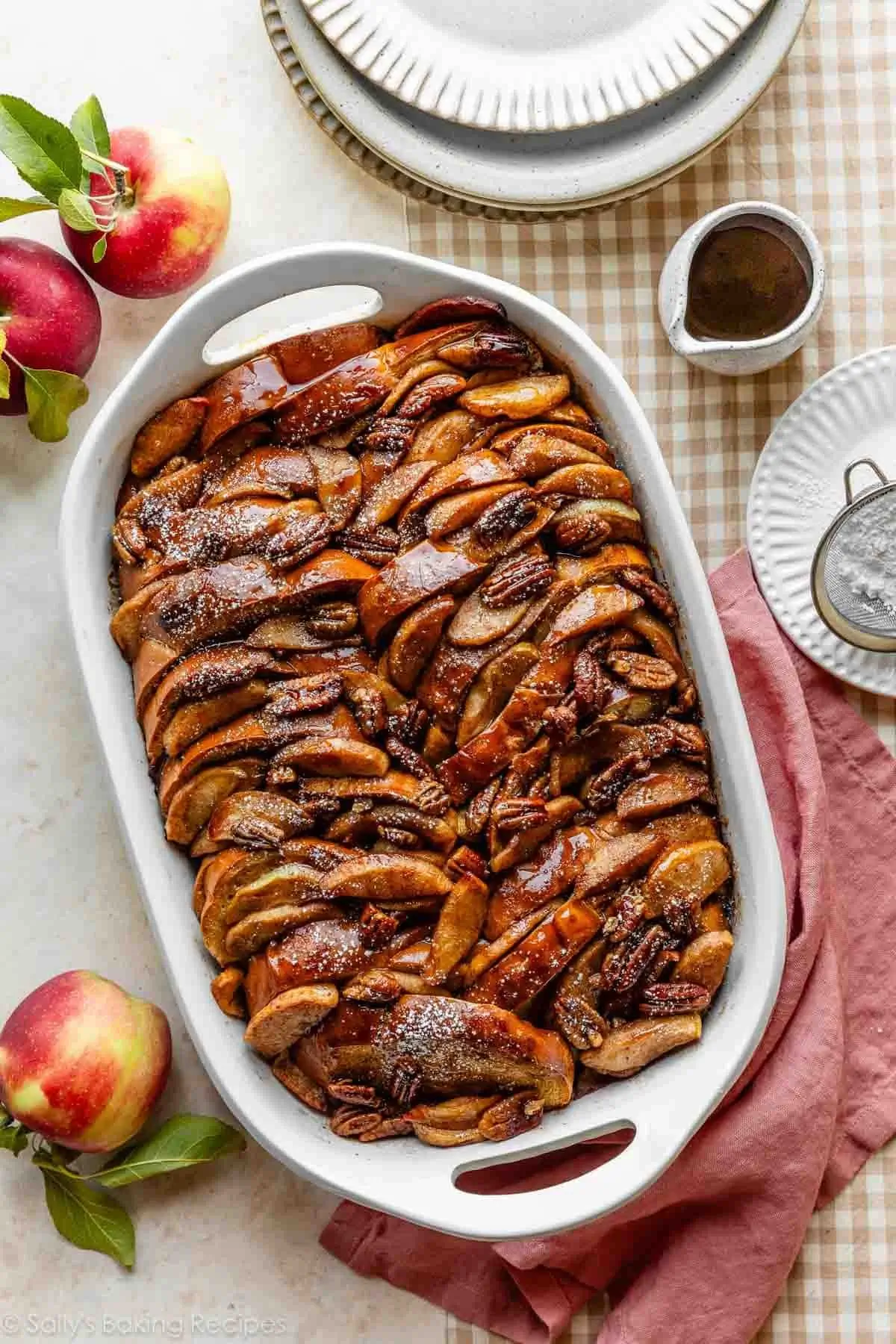 Baked apple cider French toast casserole layered with caramelized apples and pecans in a white dish.